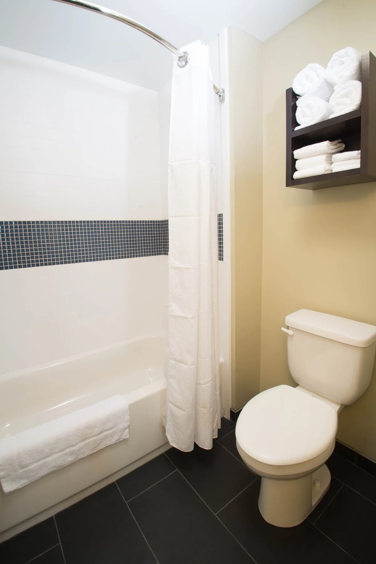 A well-lit bathroom featuring a bathtub, toilet, and neatly folded towels on a shelf. The space feels clean and inviting, offering a place to unwind after a full day of activities.