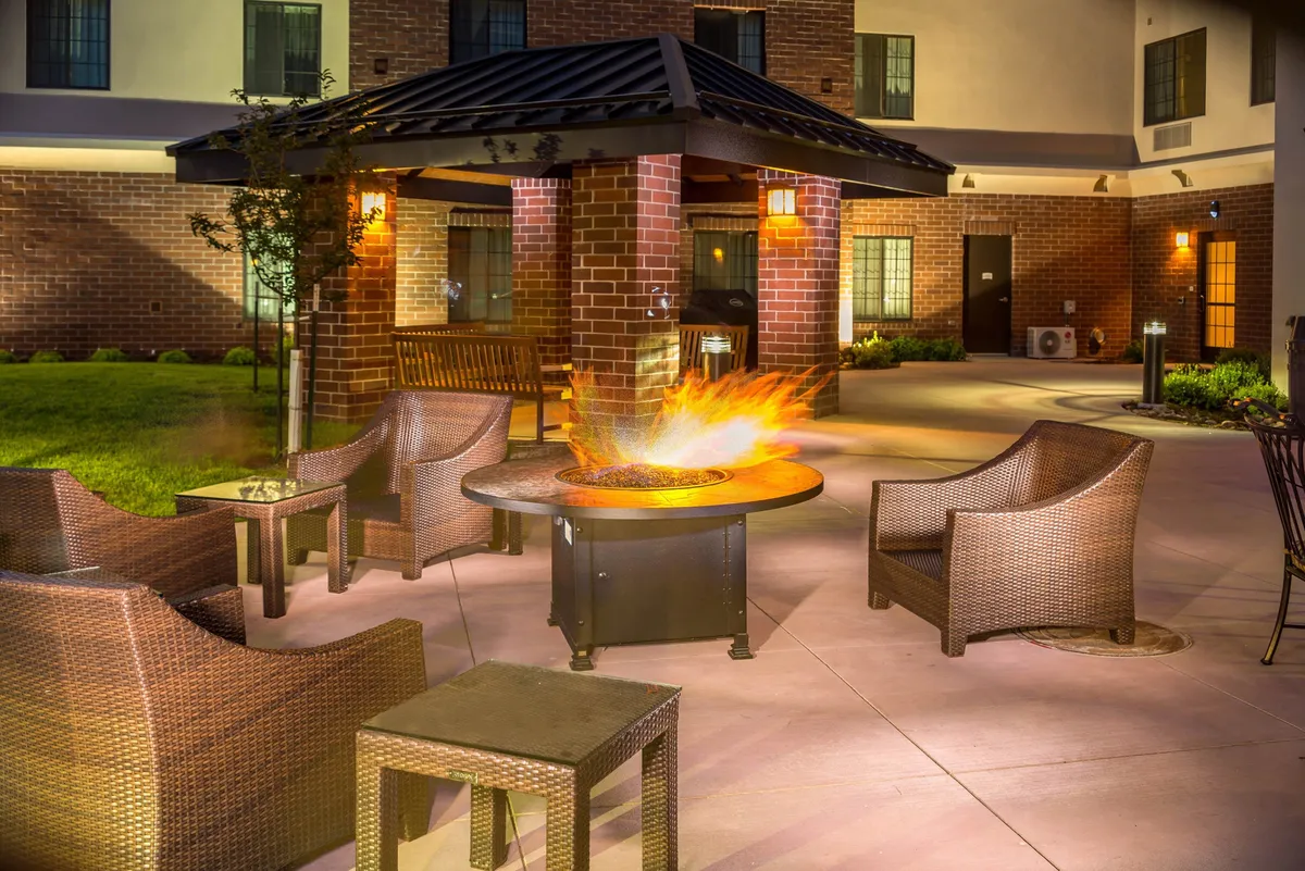 An inviting outdoor lounge area featuring a modern fire pit, comfortable wicker chairs, and a sleek canopy overhead. The setup is perfect for casual conversations or winding down in the evening after a productive workday. The open-air setting connects the property to its exterior environment, emphasizing relaxation and communal spaces.