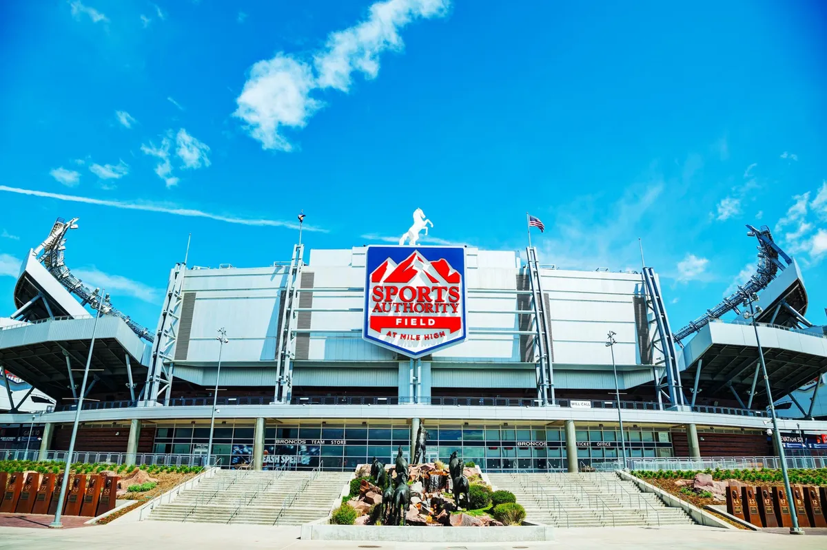 A dynamic view of Sports Authority Field, showcasing the stadium's impressive architecture and vibrant signage amidst lush landscaping. The scene hints at the excitement and energy of local events, offering a glimpse of nearby attractions easily accessible from the property.