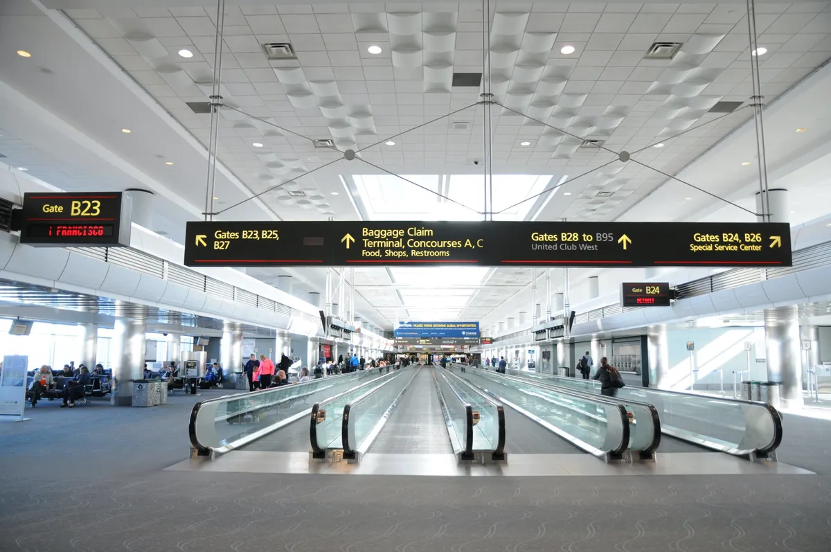 A spacious, modern interior with prominent gate signs, moving walkways, and guests comfortably waiting or moving through the space. The overall atmosphere is efficient and welcoming, suggesting a hub of activity and service.
