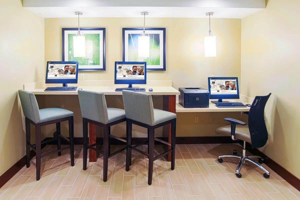 An interior workspace setup featuring computers, dedicated laptop areas, modern light fixtures, and vibrant artwork. The environment is designed to foster productivity, with amenities conducive to both focused work and informal gatherings.